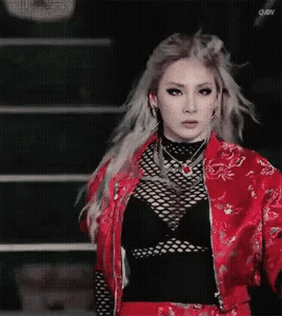 A Woman In A Red Jacket And Black Top Is Standing In Front Of A Staircase . GIF