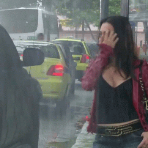 A Woman In A Red Jacket Covering Her Face In Front Of A Yellow Car GIF