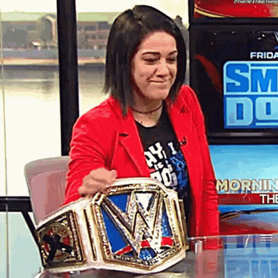 A Woman In A Red Jacket Holding A Wrestling Championship Belt GIF