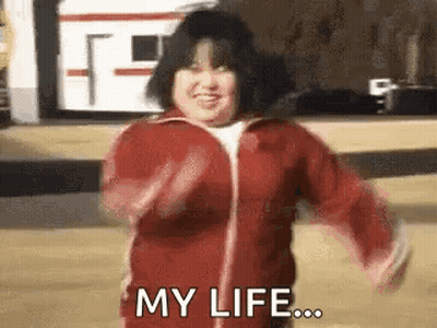 A Woman In A Red Jacket Is Dancing And Smiling While Saying `` My Life ... '' . GIF