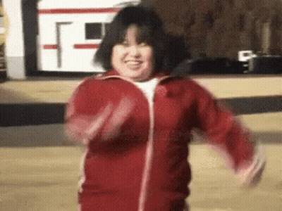A Woman In A Red Jacket Is Dancing In Front Of A Bus . GIF