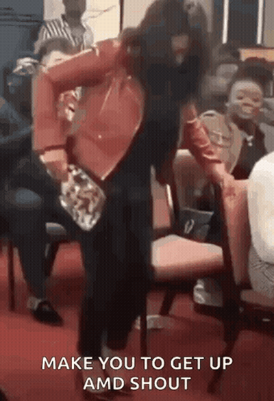 A Woman In A Red Jacket Is Dancing In Front Of A Crowd While Holding A Purse . GIF