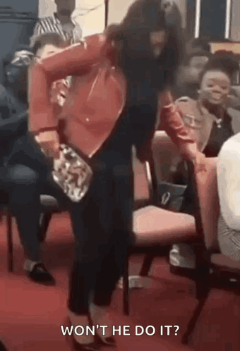A Woman In A Red Jacket Is Dancing In Front Of A Crowd While Holding A Purse . GIF