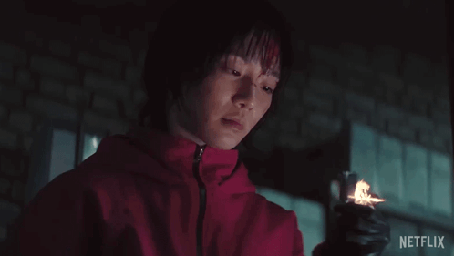 A Woman In A Red Jacket Is Holding A Lighter With Netflix Written On The Bottom Right GIF