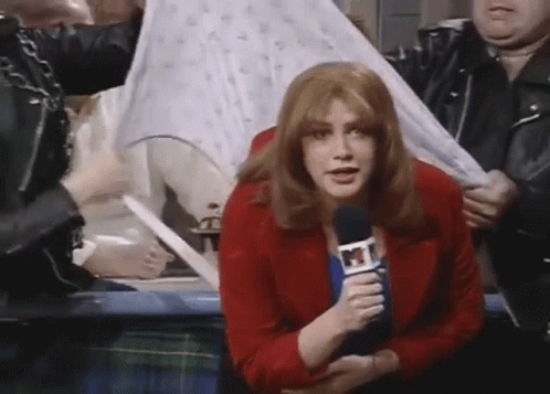 A Woman In A Red Jacket Is Holding A Microphone And Talking Into It GIF