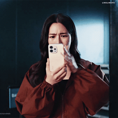 A Woman In A Red Jacket Is Looking At Her Phone And Making A Face GIF