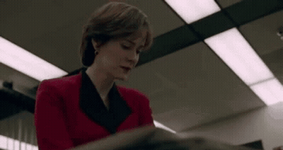 A Woman In A Red Jacket Is Sitting At A Table Reading A Book . GIF