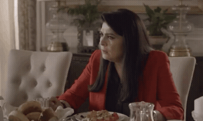 A Woman In A Red Jacket Is Sitting At A Table With A Plate Of Food GIF