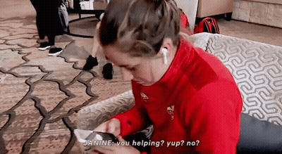 A Woman In A Red Jacket Is Sitting On A Couch Looking At Her Phone And Says " Janine You Helping " GIF