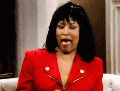 A Woman In A Red Jacket Is Sitting On A Couch With Her Mouth Open GIF