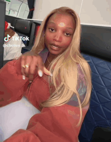 A Woman In A Red Jacket Is Sitting On A Plane With A Tiktok Watermark GIF