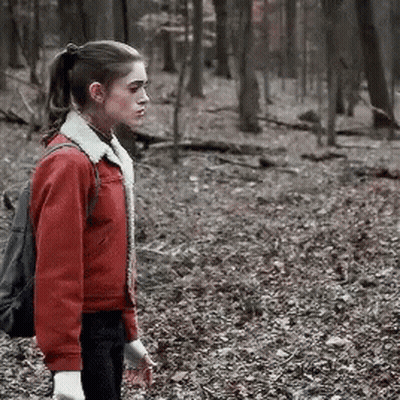 A Woman In A Red Jacket Is Standing In The Woods . GIF