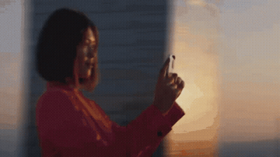 A Woman In A Red Jacket Is Taking A Picture Of The Sunset With Her Phone GIF