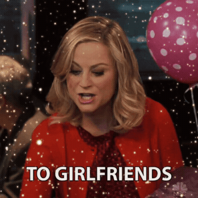 A Woman In A Red Jacket Says To Girlfriends In Front Of Pink Balloons GIF