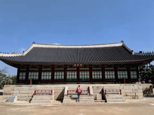 A Woman In A Red Jacket Stands In Front Of A Building GIF