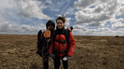 A Woman In A Red Jacket Stands Next To A Man In A Black Jacket Giving A Thumbs Up GIF