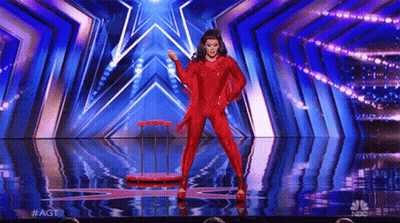 A Woman In A Red Jumpsuit Is Dancing On A Stage With A Star In The Background . GIF