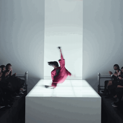 A Woman In A Red Jumpsuit Is Doing A Trick On A White Podium GIF