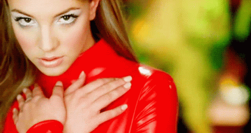 A Woman In A Red Latex Outfit Is Holding Her Hands On Her Chest . GIF