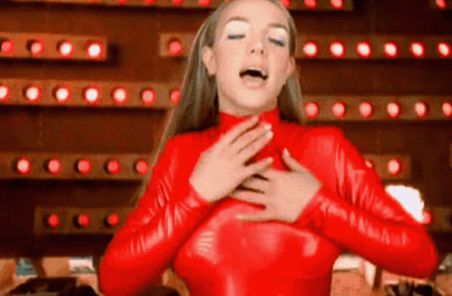 A Woman In A Red Latex Outfit Is Singing Into Her Mouth . GIF