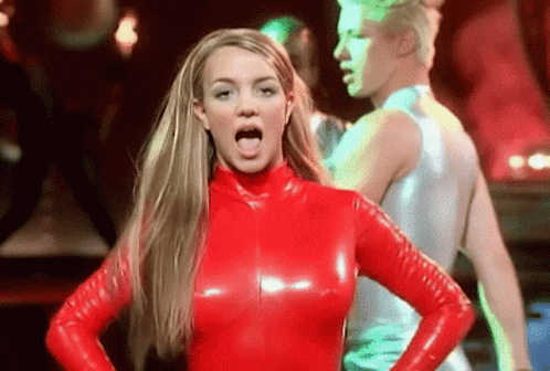 A Woman In A Red Latex Outfit Is Sticking Her Tongue Out While Standing In Front Of A Man . GIF