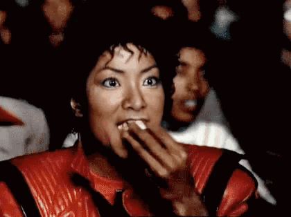 A Woman In A Red Leather Jacket Is Eating A Piece Of Food . GIF