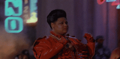 A Woman In A Red Leather Jacket Is Standing In Front Of A Neon Sign That Says ' J ' On It GIF