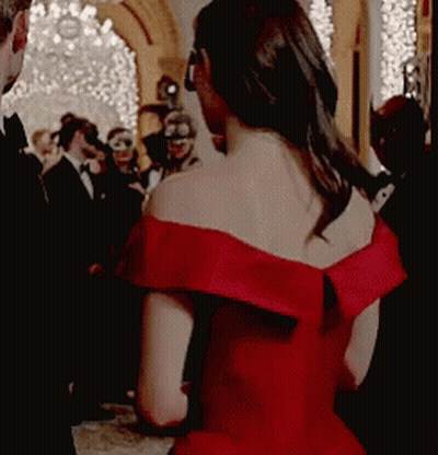 A Woman In A Red Off The Shoulder Dress Is Standing In Front Of A Crowd . GIF