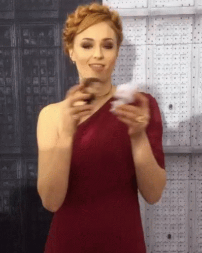 A Woman In A Red One Shoulder Dress Is Holding A Card GIF