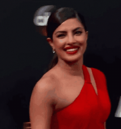 A Woman In A Red One Shoulder Dress Is Smiling And Looking At The Camera . GIF