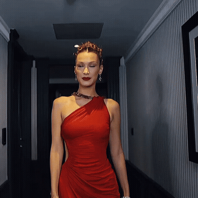 A Woman In A Red One Shoulder Dress Walks Down A Hallway GIF