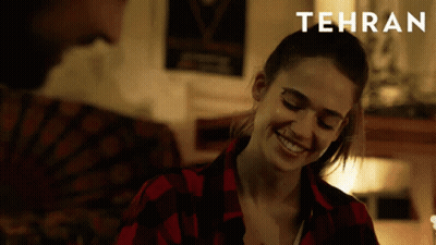 A Woman In A Red Plaid Shirt Is Smiling And Tehran Is Written Above Her GIF