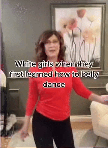 A Woman In A Red Shirt And Black Pants Is Dancing In Front Of A Picture Of Flowers . GIF