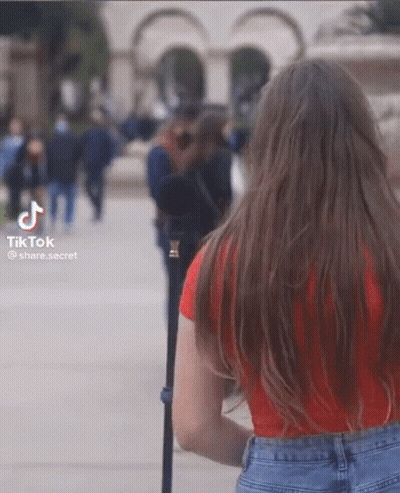 A Woman In A Red Shirt And Blue Jeans Is Walking Down The Street GIF