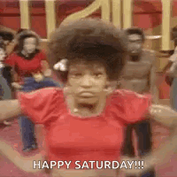 A Woman In A Red Shirt Is Dancing In Front Of A Group Of People And Saying Happy Saturday . GIF