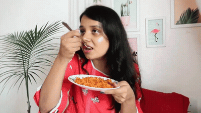 A Woman In A Red Shirt Is Eating A Plate Of Food With A Spoon GIF