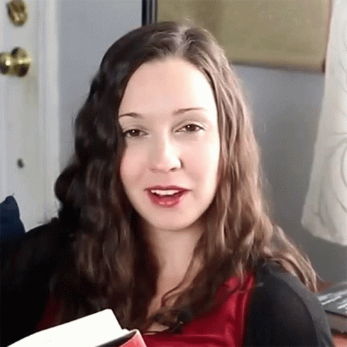 A Woman In A Red Shirt Is Holding A Book GIF