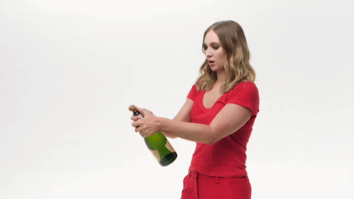 A Woman In A Red Shirt Is Holding A Bottle Of Champagne GIF