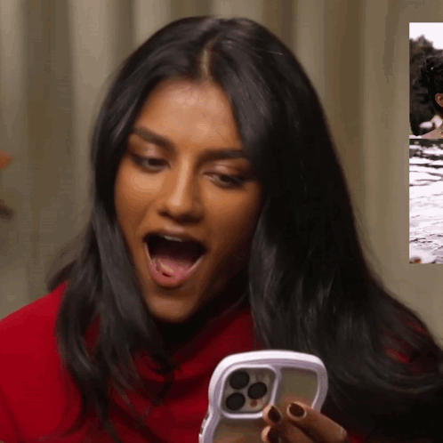 A Woman In A Red Shirt Is Holding A Cell Phone With Her Mouth Open GIF