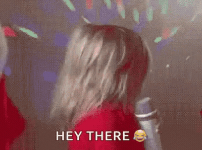 A Woman In A Red Shirt Is Holding A Microphone And Says Hey There . GIF