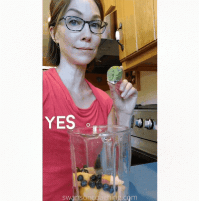 A Woman In A Red Shirt Is Holding A Piece Of Fruit In Front Of A Blender That Says Yes GIF