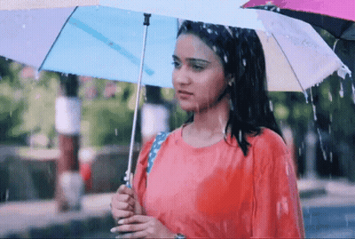 A Woman In A Red Shirt Is Holding An Umbrella While Standing In The Rain GIF
