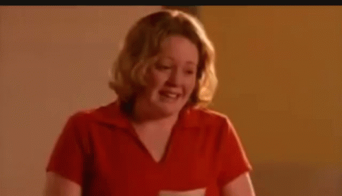 A Woman In A Red Shirt Is Laughing And Looking Down . GIF