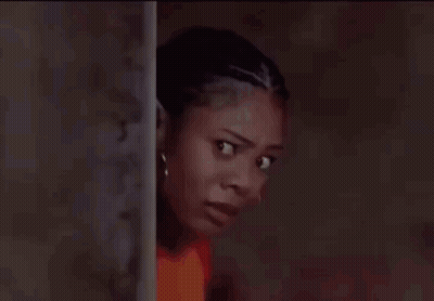 A Woman In A Red Shirt Is Leaning Against A Wall And Looking At The Camera . GIF