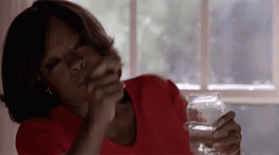 A Woman In A Red Shirt Is Sitting At A Table Holding A Glass Of Water In Her Hand . GIF