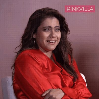 A Woman In A Red Shirt Is Sitting In Front Of A Pink Wall With Pinkvilla Written On It GIF