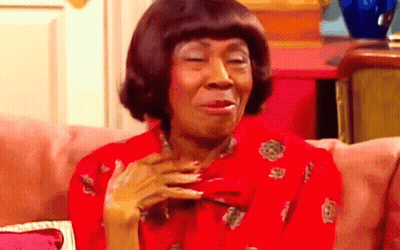 A Woman In A Red Shirt Is Sitting On A Pink Couch Making A Funny Face GIF