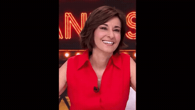 A Woman In A Red Shirt Is Smiling And Looking At The Camera . GIF