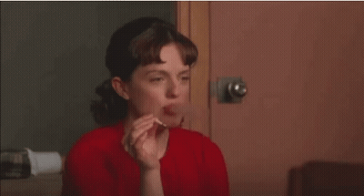 A Woman In A Red Shirt Is Smoking A Cigarette While Sitting In Front Of A Door . GIF
