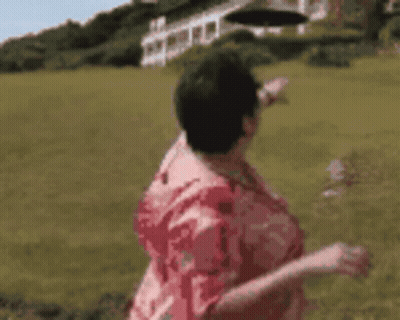 A Woman In A Red Shirt Is Standing In A Field Pointing At Something . GIF